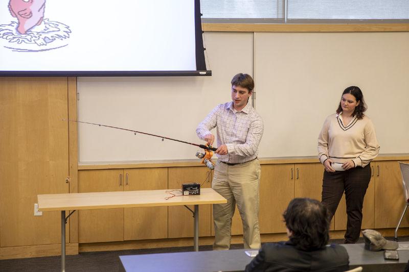 一名男学生手持自适应鱼竿向一群与会者演示
